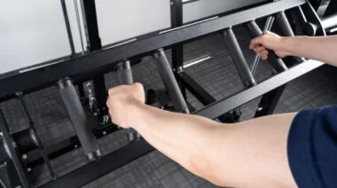 A close up image shows an athlete's hands as they grip a Swiss bar.