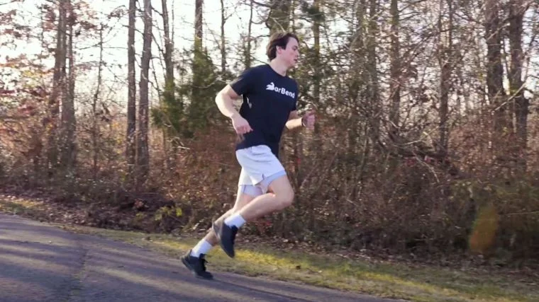A person wearing a black shirt with "BarBend" printed on the front running outside.