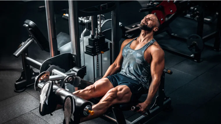 A muscular person doing leg extension exercise on the machine.