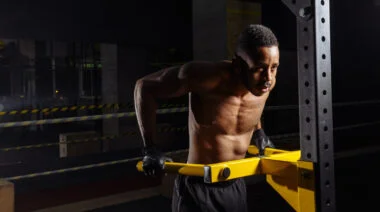 A shirtless person performs dips on a yellow dip bar.