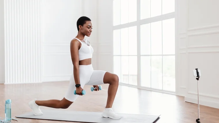 A person performs dumbbell lunges in their living room.