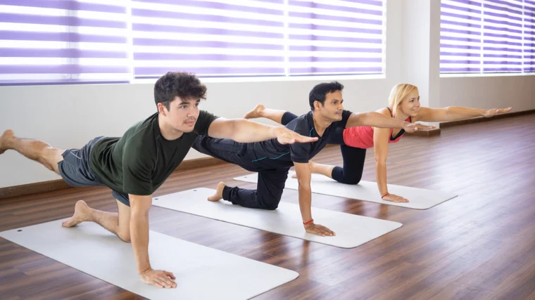 Three people perform a bird dog on yoga mats.