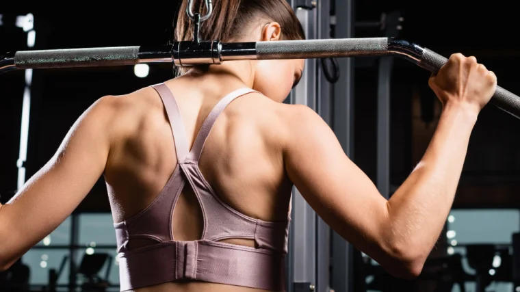 A muscular person doing lat exercise in the gym.
