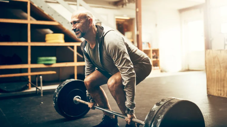 A person above 40 years old deadlifting a barbell in the gym. 