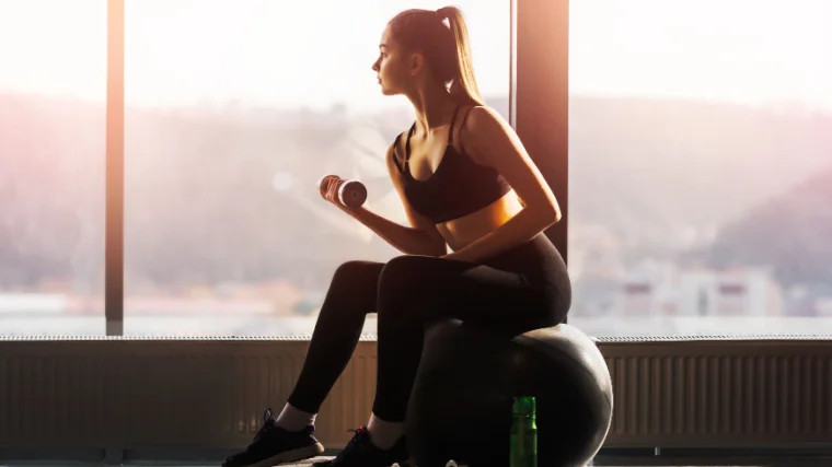 A fit person working out with a dumbbell near the window.