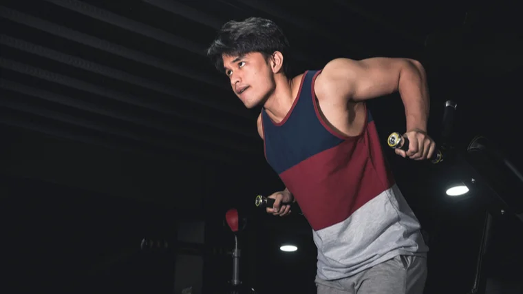 A person wearing a block-colored tank top performs dips.