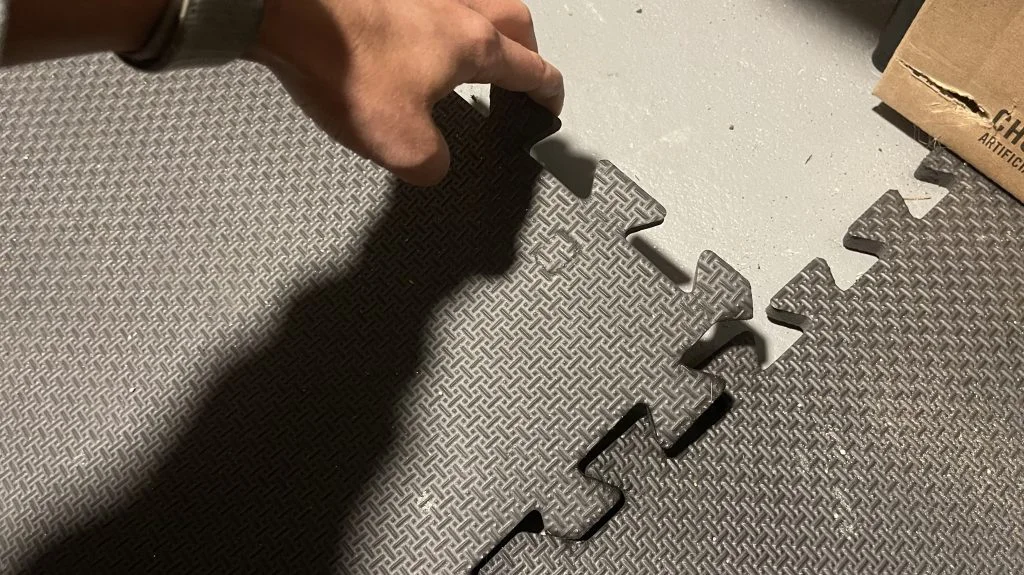 A hand lifts a section of interlocked foam puzzle flooring.