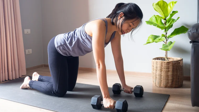 A person settles into tabletop position while holding dumbbells.