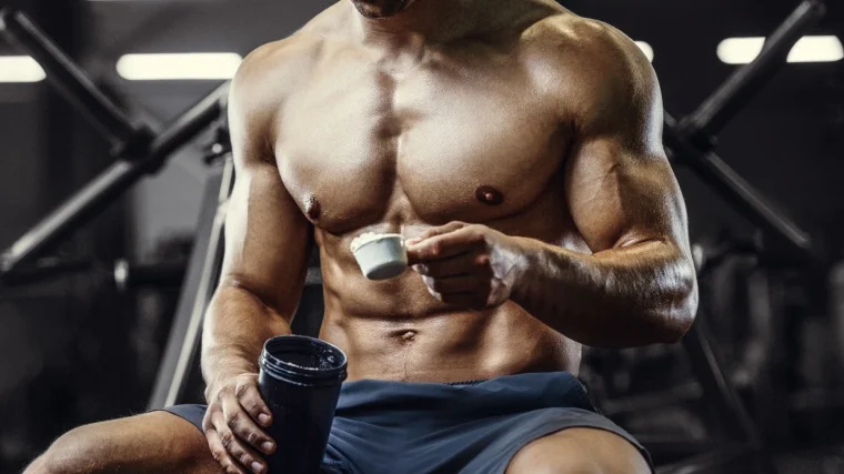 A person pouring a scoop of powdered supplement to a shaker.