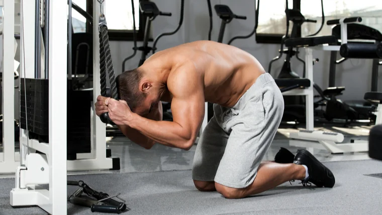 A shirtless person performs a cable crunch while facing the cable stack.