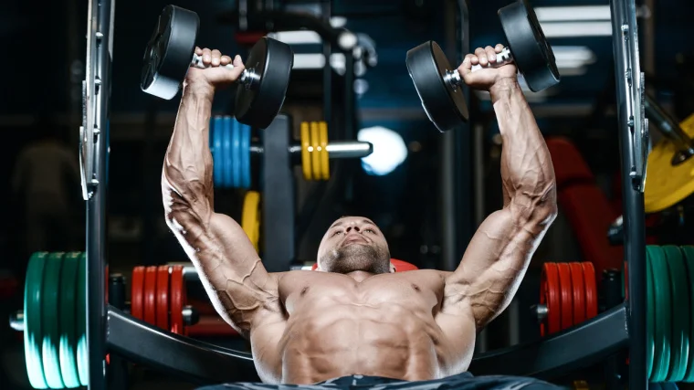 A muscular person performing the dumbbell bench press exercise in the gym.