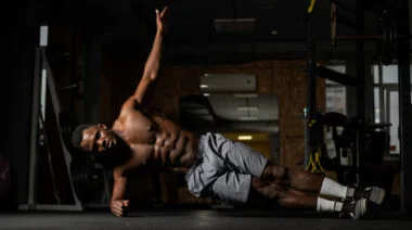 A shirtless person performs a side plank in the gym.