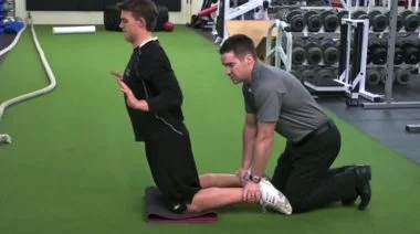 A coach helping someone do the Nordic curl.