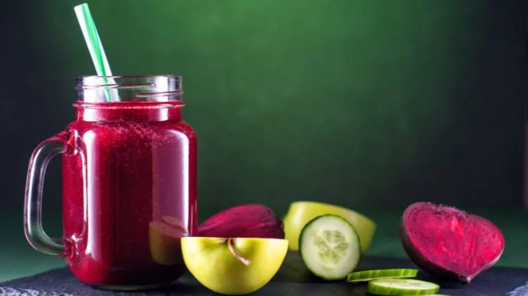 A glass of beetroot smoothie, and sliced fruits on the table.