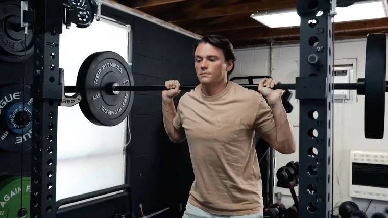 A person stands tall with a loaded barbell on their back, ready to perform back squats.