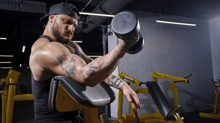 A bodybuilder doing a preacher curl with a dumbbell. 