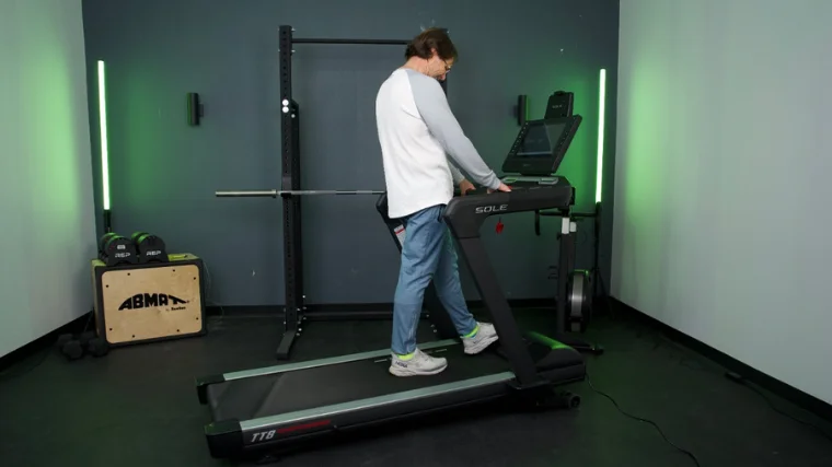 A person wearing jeans and a white long-sleeved shirt walks on the Sole TT8 Treadmill.