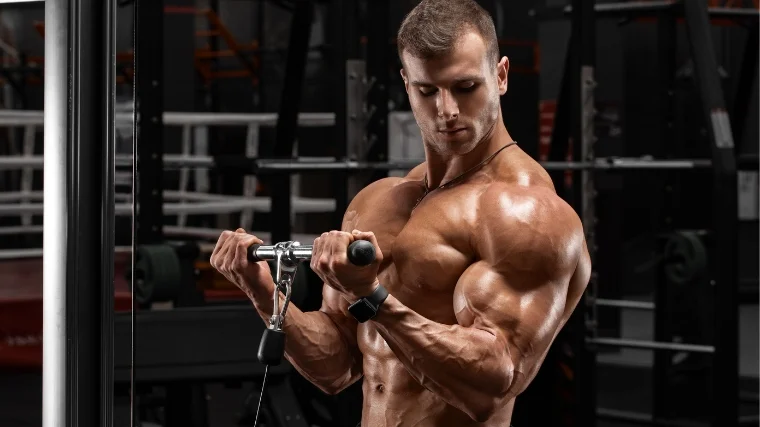 A shirtless bodybuilder doing cable biceps curls.