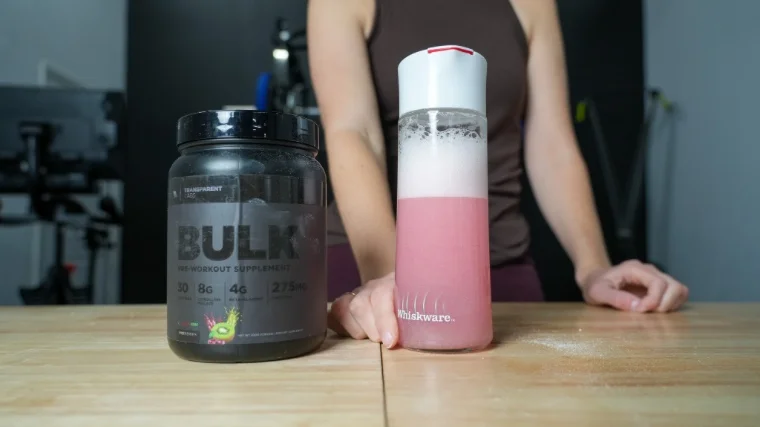 A woman stands behind a shaker glass and container of Transparent Labs Bulk Black Pre.
