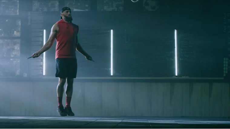A person wears a red shirt and black shorts while performing double unders.
