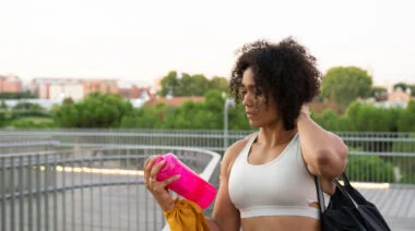 A person with curly hair shakes a protein shaker bottle on the go.
