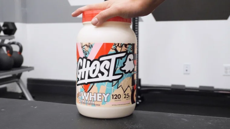 Our tester's hand on a container of Ghost Whey Protein Powder