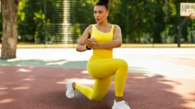 A person in a yellow tank top and leggings doing a curtsy lunge.