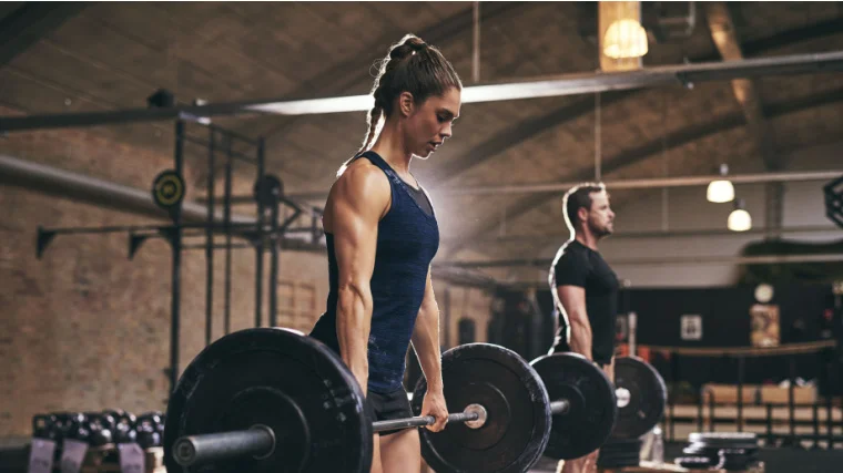 Two people working out lifting heavy barbells in the gym.