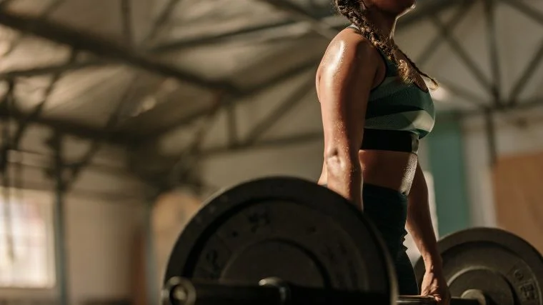 Person in camo sports bra lifting a barbell off of the floor.