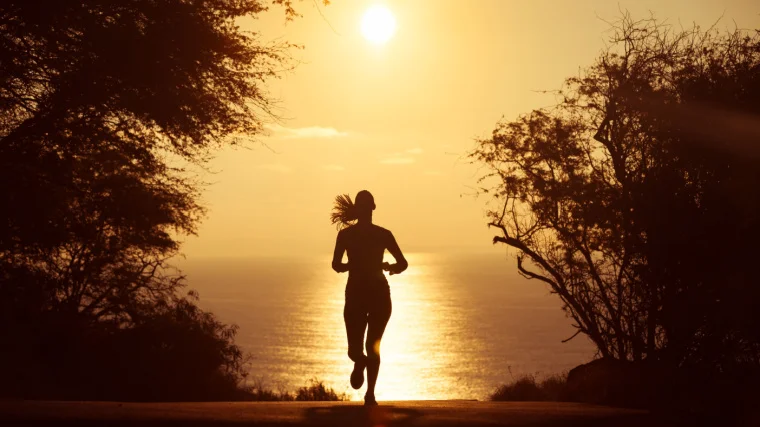 Woman silhouette running on road with sun low in the sky