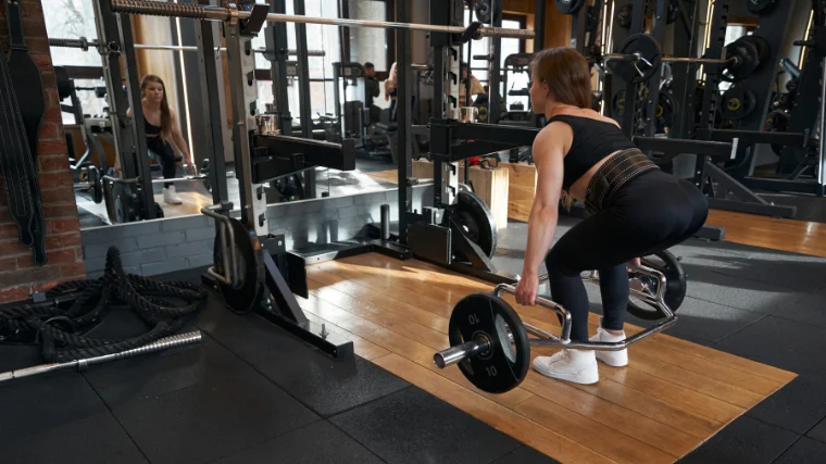 female athlete performs belted trap bar deadlift on platform
