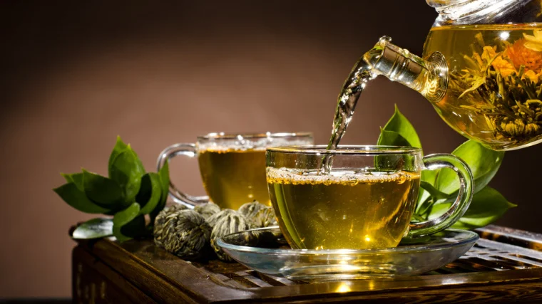 Two cups full of green tea poured from a glass teapot.