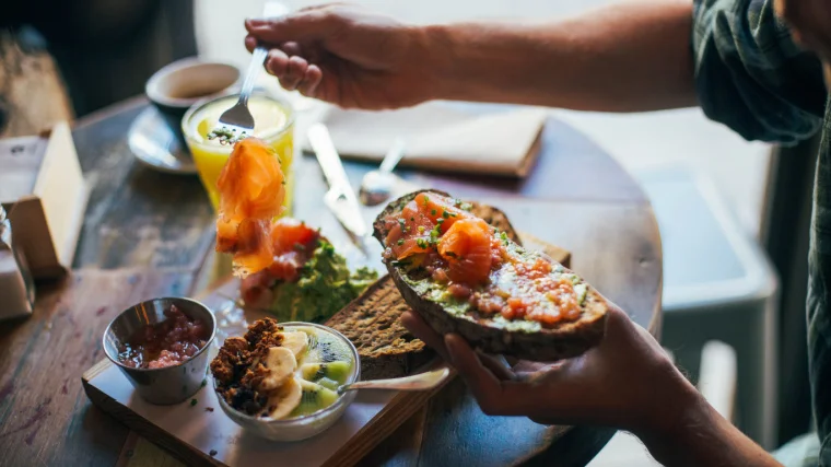 A person enjoys a big and tasty breakfast of delicious sandwich or toast with avocado spread and smoked salmon on top.