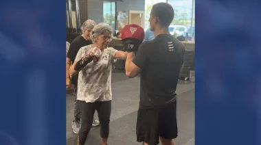 An elderly woman spars with a gym employee
