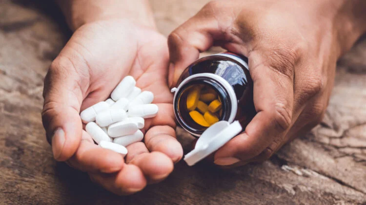 person holding a pill bottle with capsules in the other hand