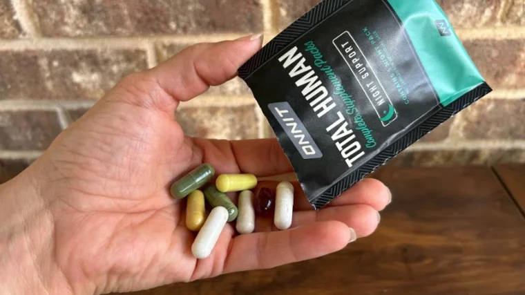 onnit-total-human-pouring A person holds a packet of Onnit Total Human along with the multivitamins themselves.