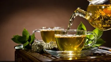Two cups full of green tea poured from a glass teapot.