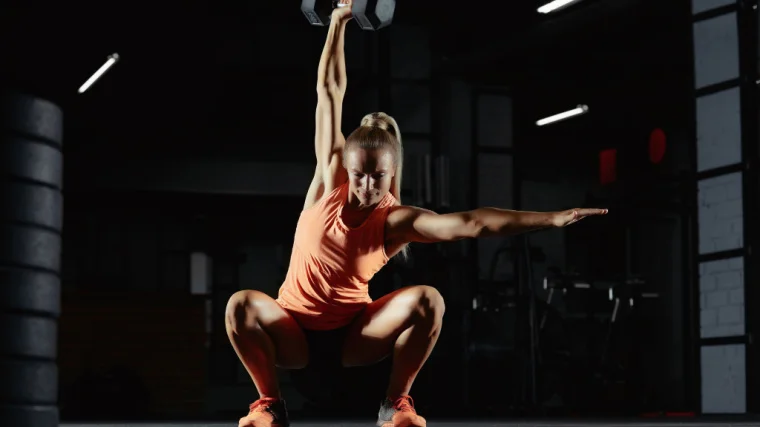 A person performs a one-arm dumbbell overhead squat to full depth.