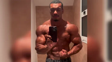 Shirtless bodybuilder posing in a mirror.