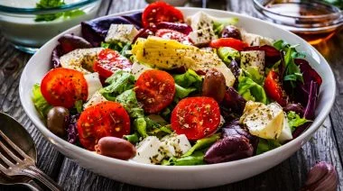 Fresh Greek salad - feta cheese, cherry tomatoes, artichokes, lettuce, black olives and onion on wooden table.