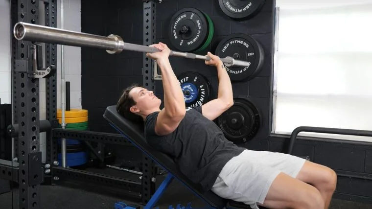 A person performing the incline barbell bench press exercise.