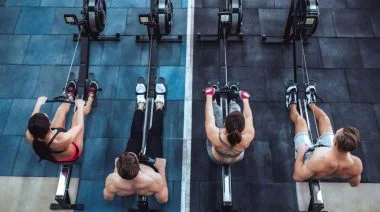 Group of sporty muscular people working out on a rowing machine in the gym.