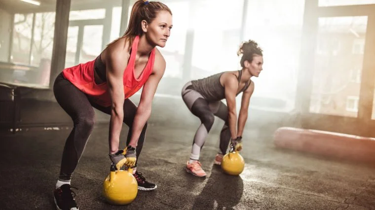Two people doing kettlebell glute workouts in the gym.