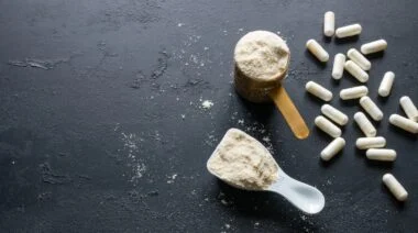 Supplement powder in two scoops and some supplement capsules on black surface.