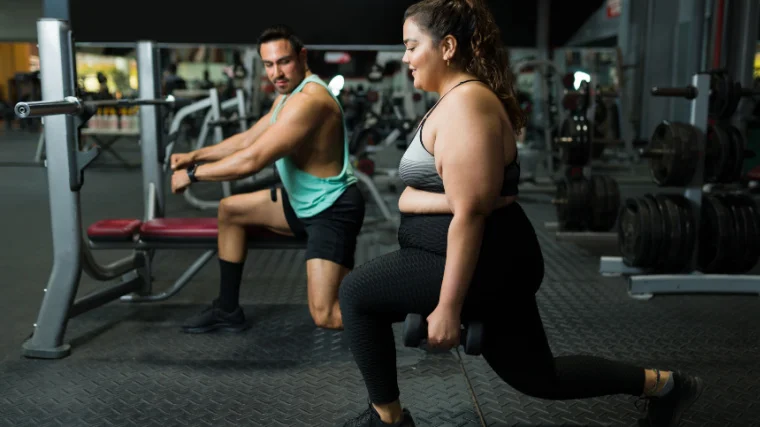 Two athletes perform lunges in the gym.