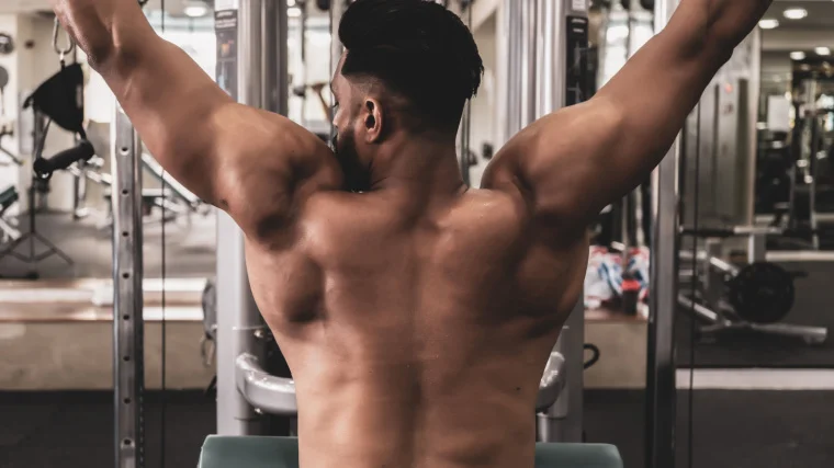 A shirtless athlete performs a lat pulldown.