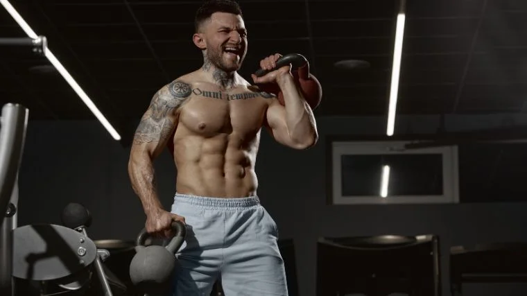 A muscular athlete carrying two kettlebells.
