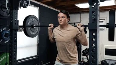 Our tester in a tan t-shirt squats with a loaded barbell draped across their back.