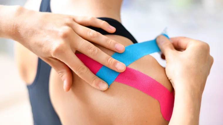 A person applying kinesiology tape on someone's shoulder.