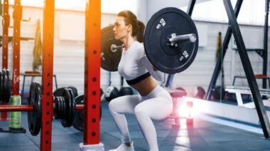 A person performs a low bar back squat in the gym.